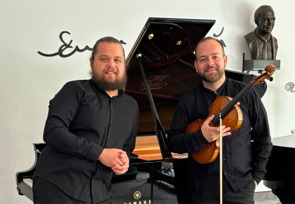 Vojtech Bélu Botoš and Vladyslav Panchenko pose for a photograph, standing next to a piano. Violový recitál Zaostrené na violu.